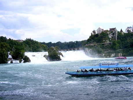 Ein blaues-Rundfahrt-Boot auf dem Weg zum Rheinfall, am rechten Bildrand Schloss Laufen.