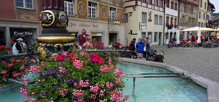 Touristen bestaunen einen mit Blumen geschmückten Brunnen in der Altstadt von Stein am Rhein.