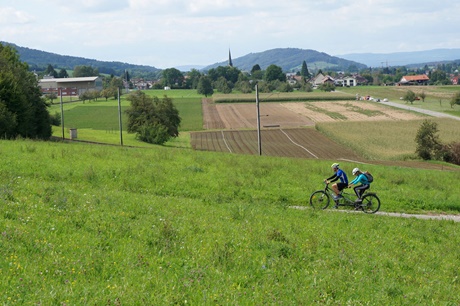 Ein Pärchen quält sich mit einem Tandem eine Anhöhe bei Eschenz hinauf (im Bildhintergrund ragt der Kirchturm der Kirche Alt-Steckborn in die Höhe).