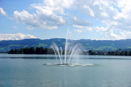 Fontäne im Bodensee bei Arbon; am gegenüberliegenden Ufer ist der Ort Wasserburg mit seiner Katholischen Pfarrkirche St. Georg zu erkennen.