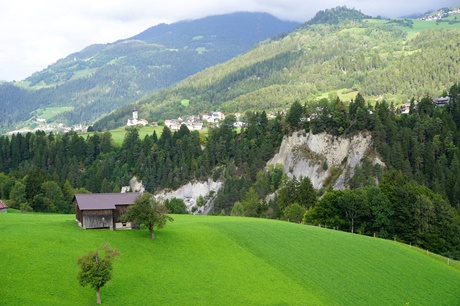 Eine bewaldete Steilwand der Rheinschlucht von der Straße nach Bonaduz aus gesehen, im HIntergrund das Dorf Sagogn.