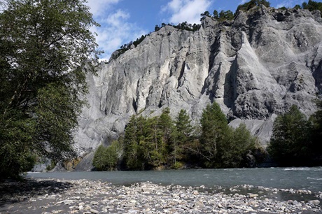 Der eine graue Steilwand passierende Rhein direkt vom Boden der Rheinschlucht aus gesehen.