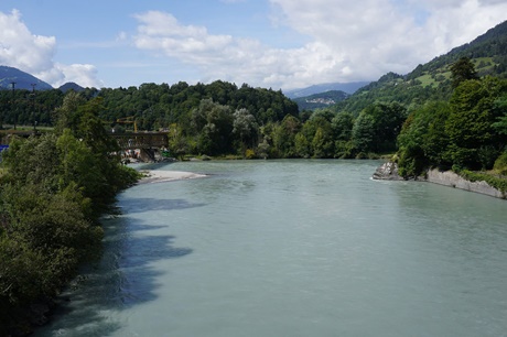 Der malerisch von Bäumen umrahmte Zusammenfluss von Hinter- und Vorderrhein bei Reichenau, am linken Bildrand die Rheinbrücke von Tamins.