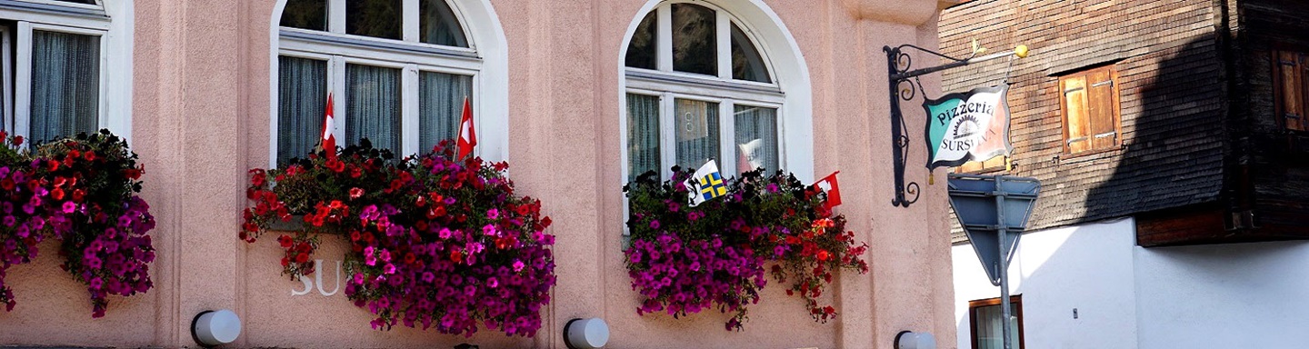 Mit Blumen und Schweizer Flaggen geschmückte Fassade der Pizzeria Surselva in Disentis.