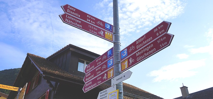 Roter Wegweiser an einer Kreuzungsstelle von Rhein-, Rhone- und Nord-Süd-Route in Andermatt.